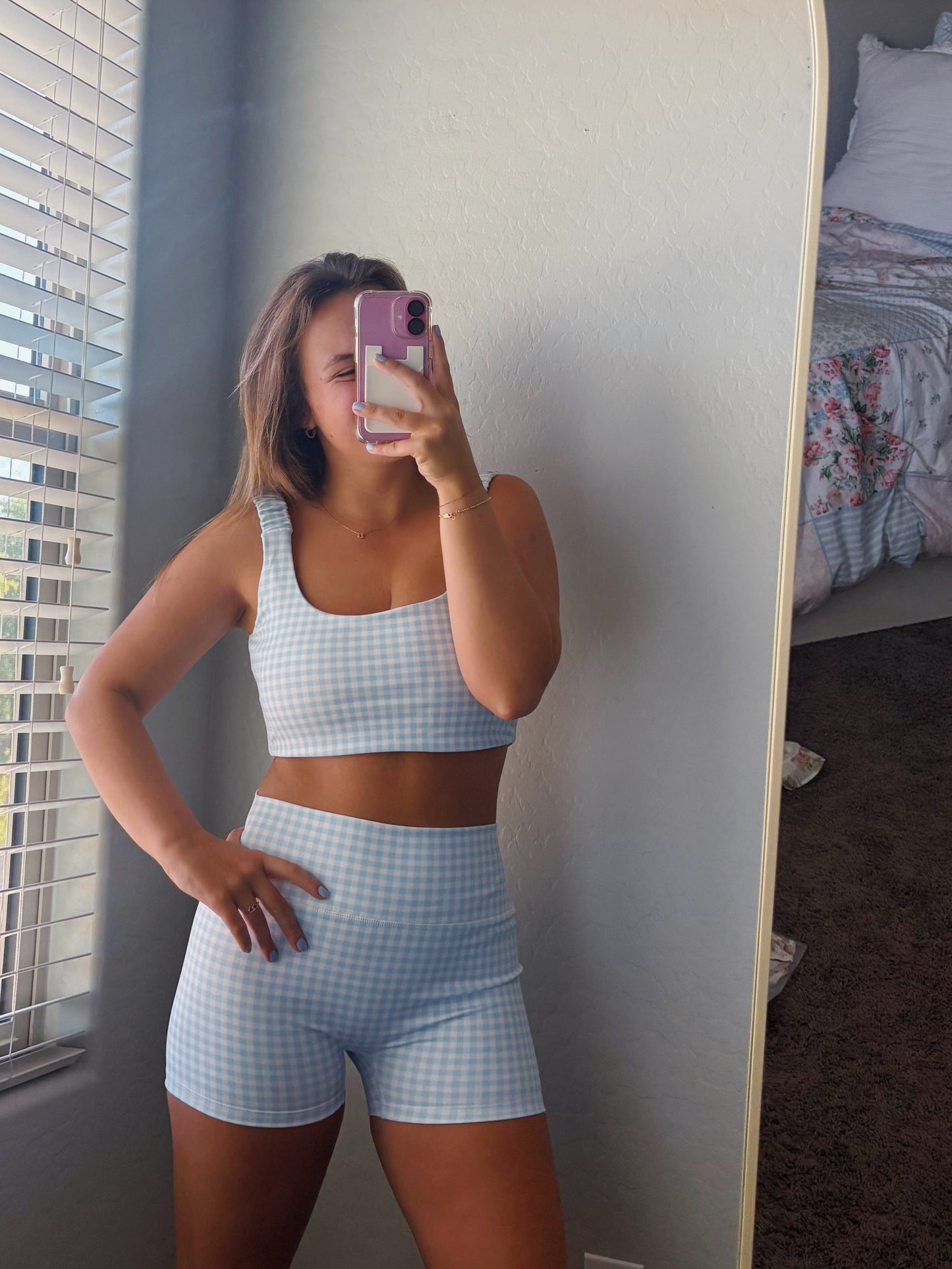 Person taking a mirror selfie wearing a light blue athletic outfit in a bedroom.