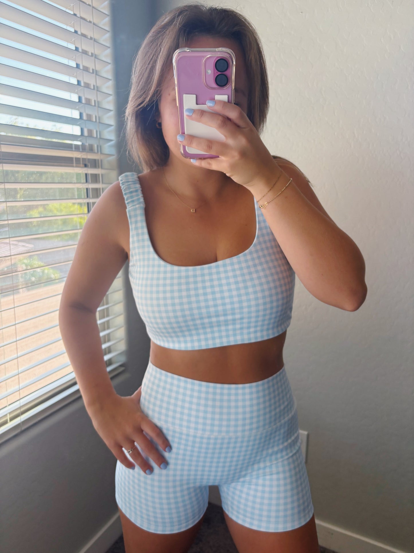 Person wearing a light blue checkered sports bra and shorts in front of a window.