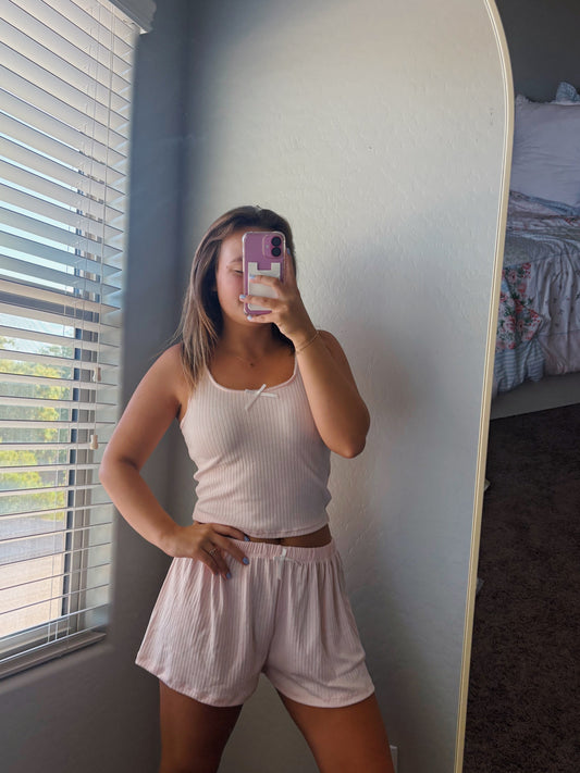Person taking a mirror selfie wearing a white tank top and shorts in a bedroom.